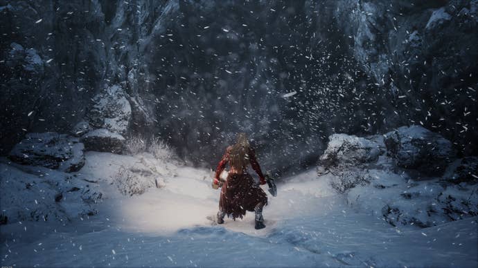 Players stand in the snow outside a cave.