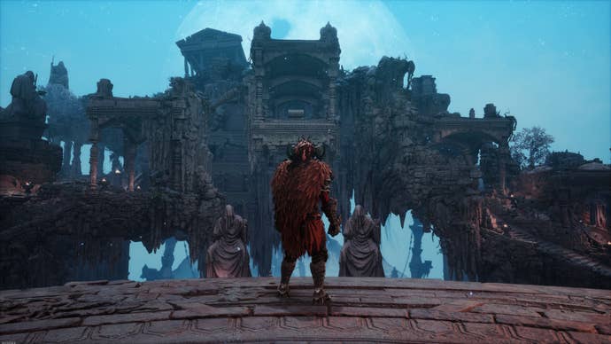 The player wears a red cloak and stands on a platform to look at some ruins.